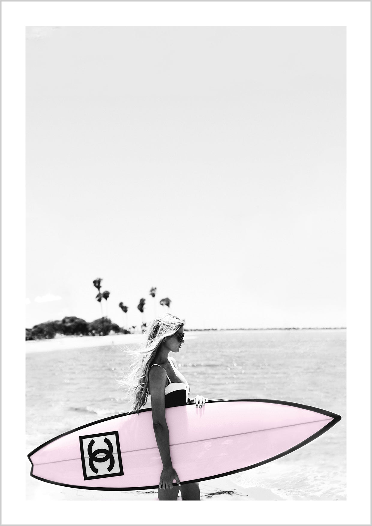 Photograph of a bikini girl holding a pink Chanel surfboard toward the sea.