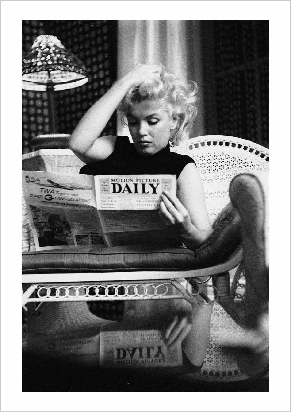 Black & White photography Poster with an iconic photo of Marylin Monroe reading a daily newspaper on the sofa at her home.