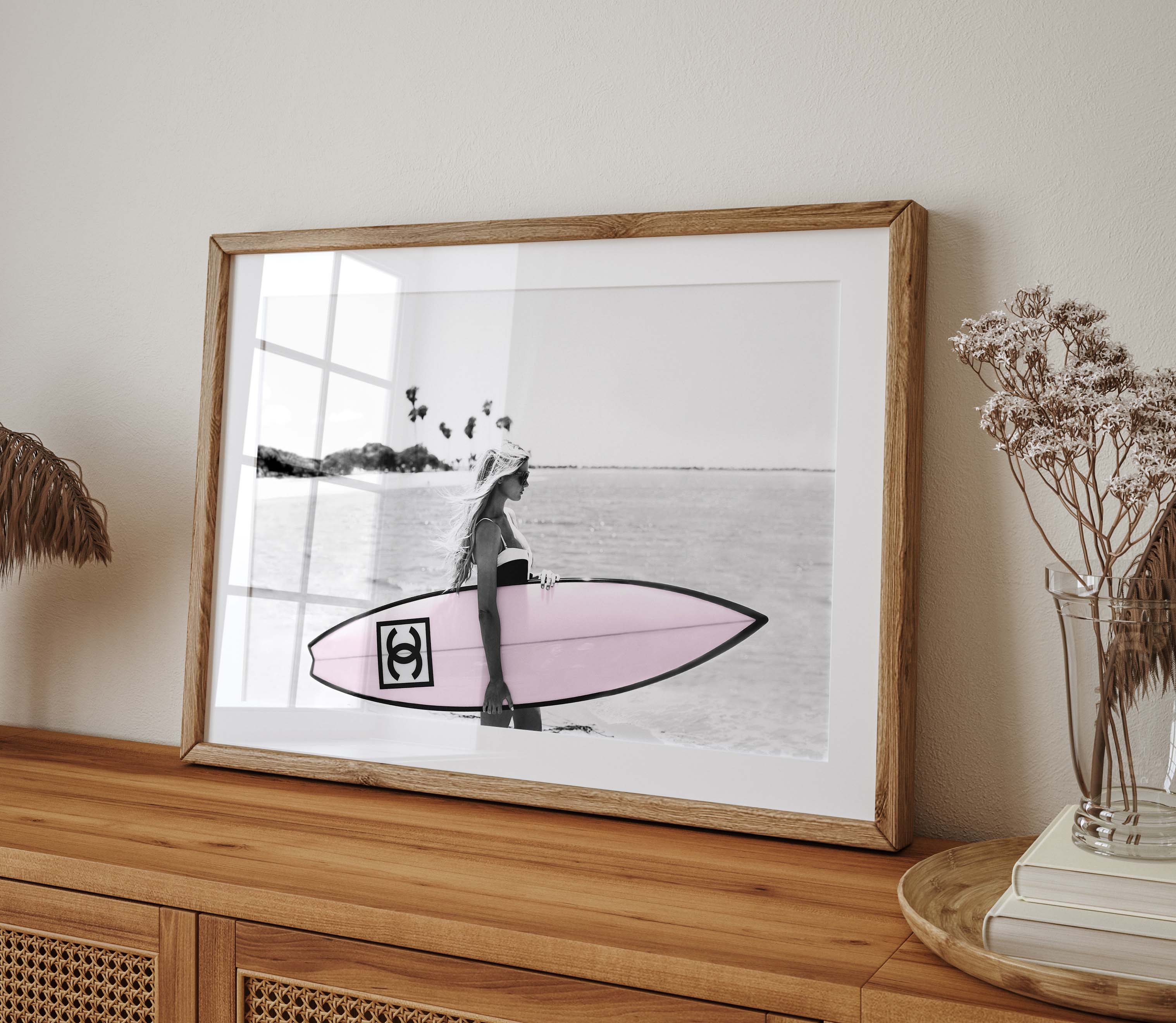 Photograph of a bikini girl holding a Chanel surfboard toward the sea.