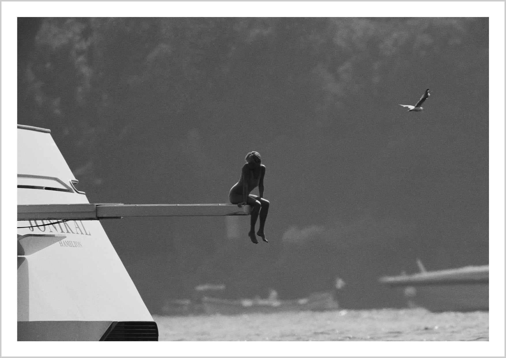 A figure sitting on the edge of a boat, overlooking a tranquil body of water with a bird in flight nearby. – Arteve Gallery