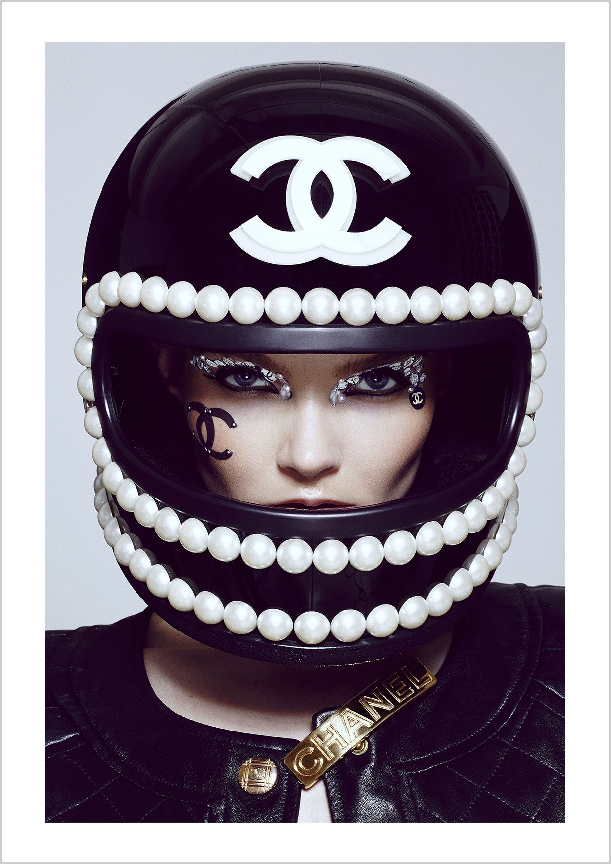 Close-up of a person wearing a black helmet adorned with pearls and Chanel logos, with dramatic makeup. – Arteve Gallery