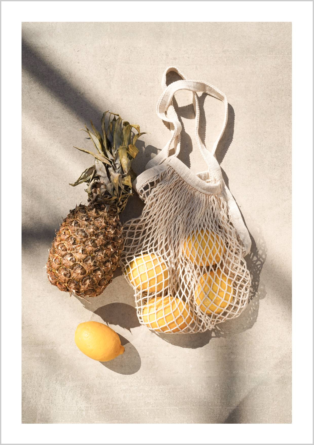 A pineapple and a bag of lemons on a light surface, with soft shadows. – Arteve Gallery