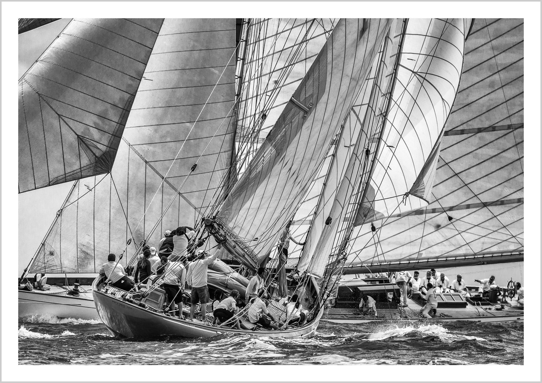 A black and white image of sailboats racing on water, with crew members actively maneuvering the sails. – Arteve Gallery