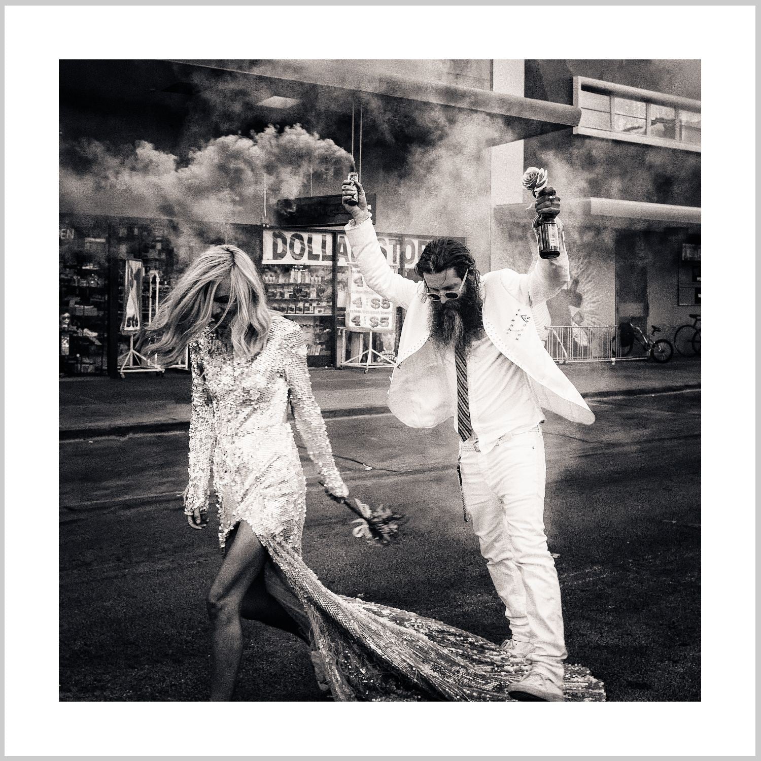 A couple in wedding attire walking through a smoky urban street, with the man holding a microphone and the woman carrying a bouquet. – Arteve Gallery