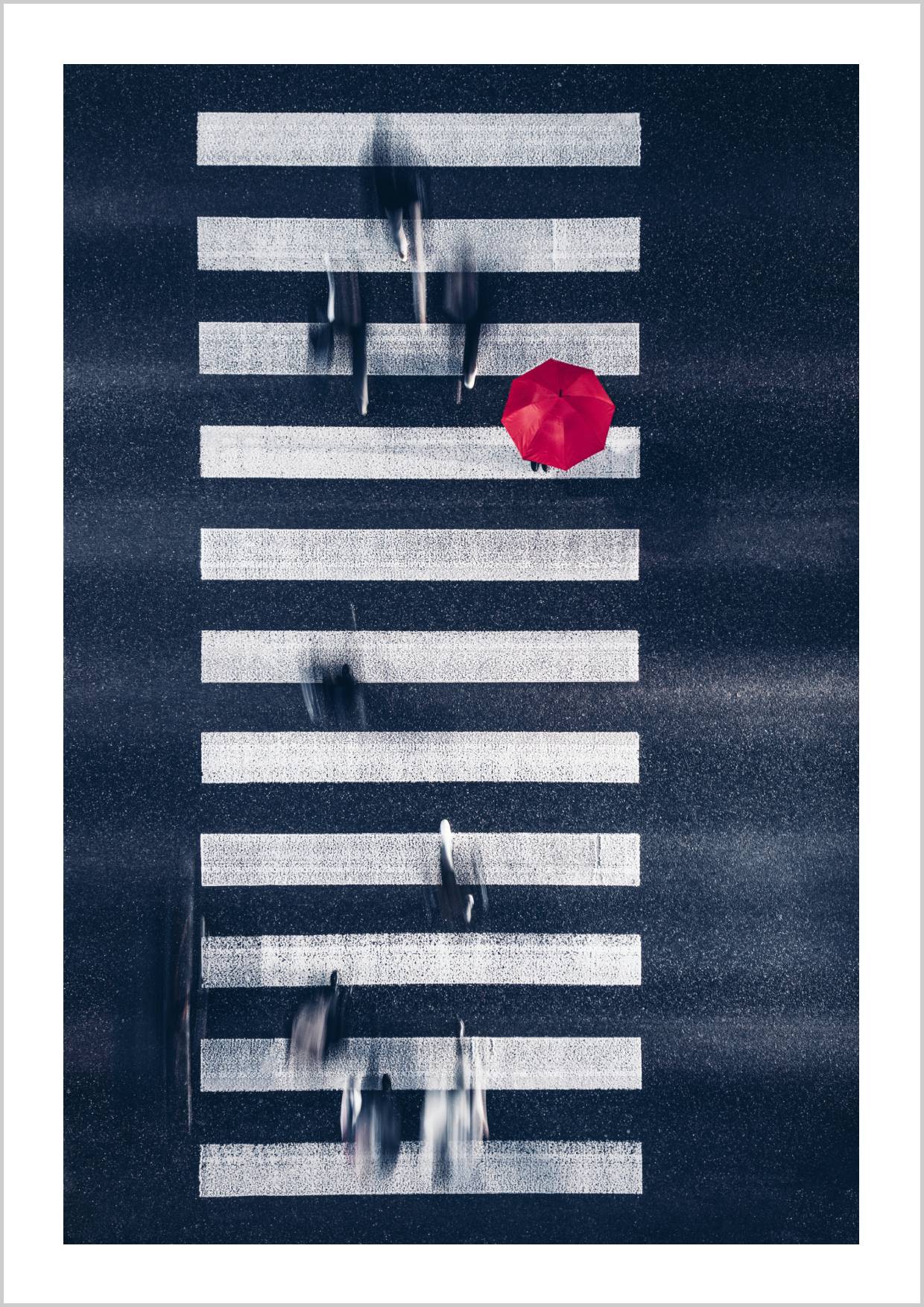 An aerial view of a busy pedestrian crossing with a red umbrella amidst blurred figures and white stripes. – Arteve Gallery