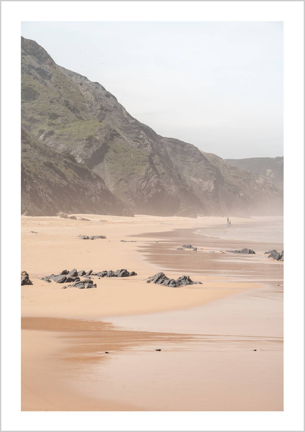 A misty coastal landscape featuring sandy beach, rocky cliffs, and gentle waves under a hazy sky. – Arteve Gallery