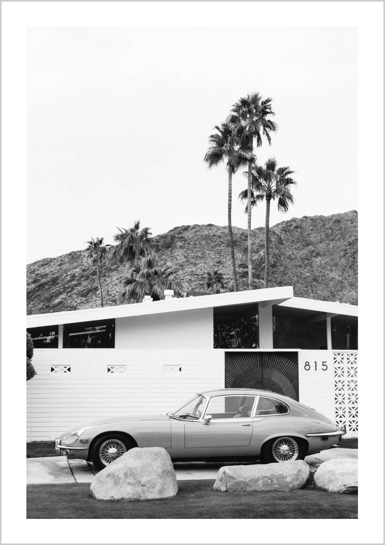 A vintage car parked in front of a mid-century modern building surrounded by palm trees and mountains. – Arteve Gallery