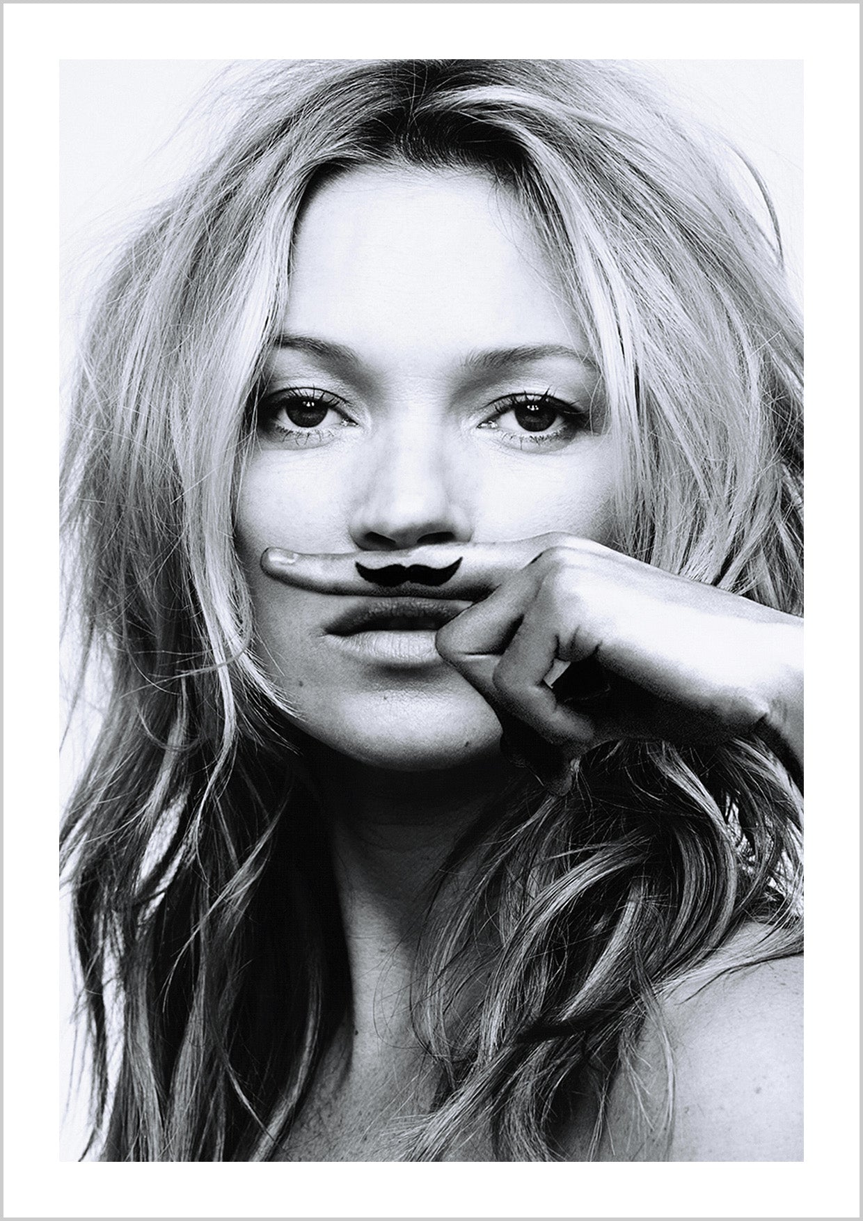 Black and white photograph of Kate Moss with a finger above her mouth with a moustache on the finger