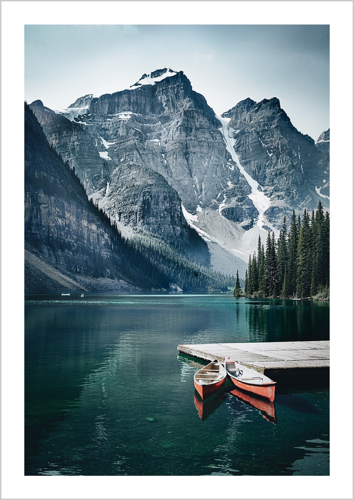 Nature poster with a photographic motif of two red canoes resting on a picturesque wooden pier on a quiet lake. On the side of the clear-blue lake, tall, ice-clad mountains are towering which is reflected beautifully on the still water surface.