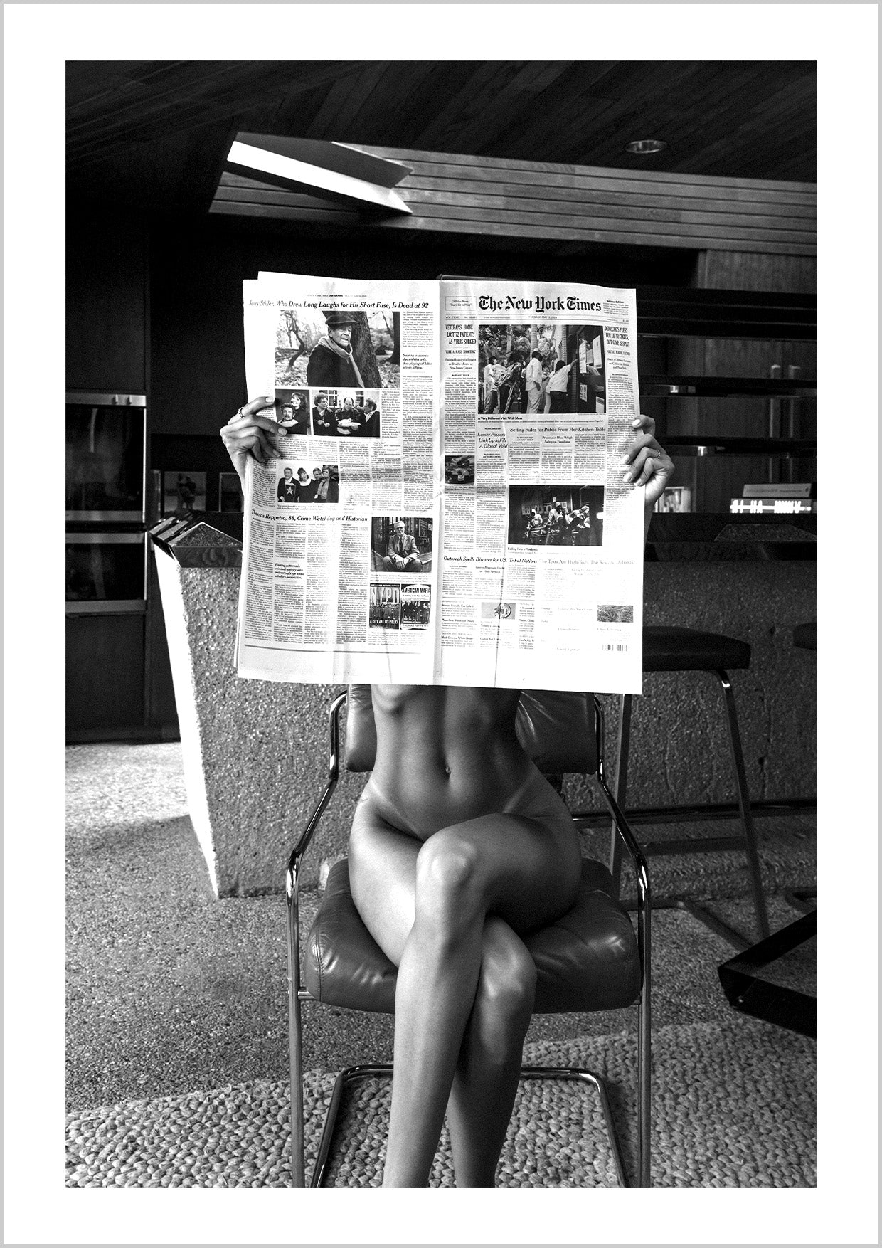 Photograph of a nude woman sitting on dining table reading newspaper