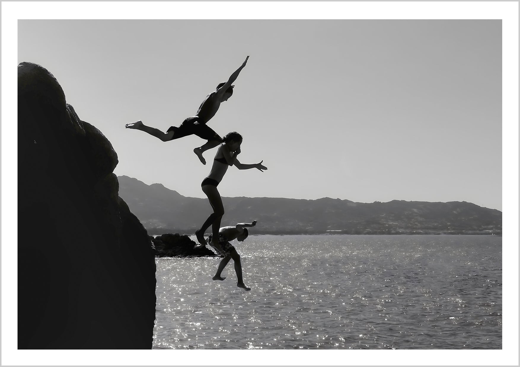 Black and white poster of 3 kids jumping into the sea from a Clift