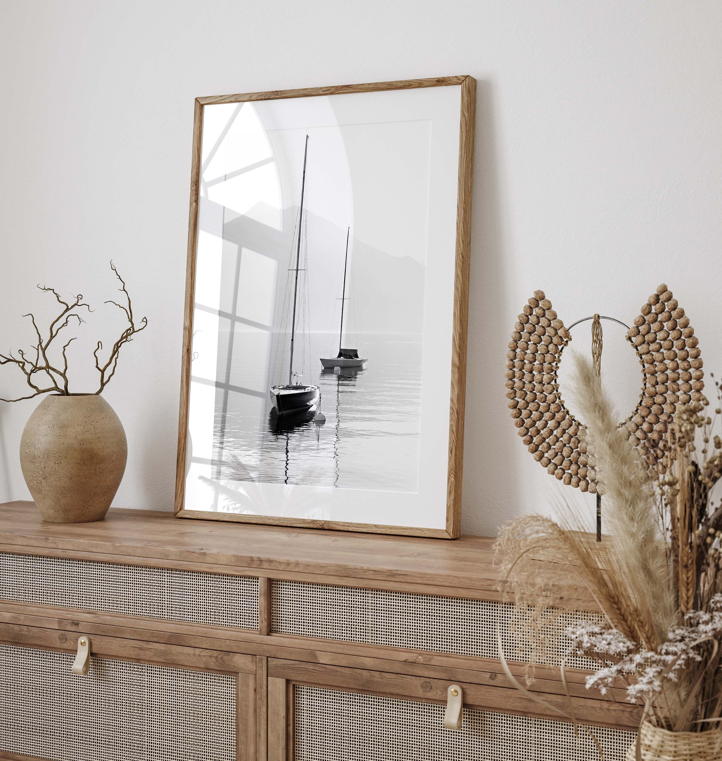Harmonic photo poster in black and white with motifs of two sailboats floating peacefully on a calm sea. In the background, the silhouette of an angular mountain stretches toward the grey sky.