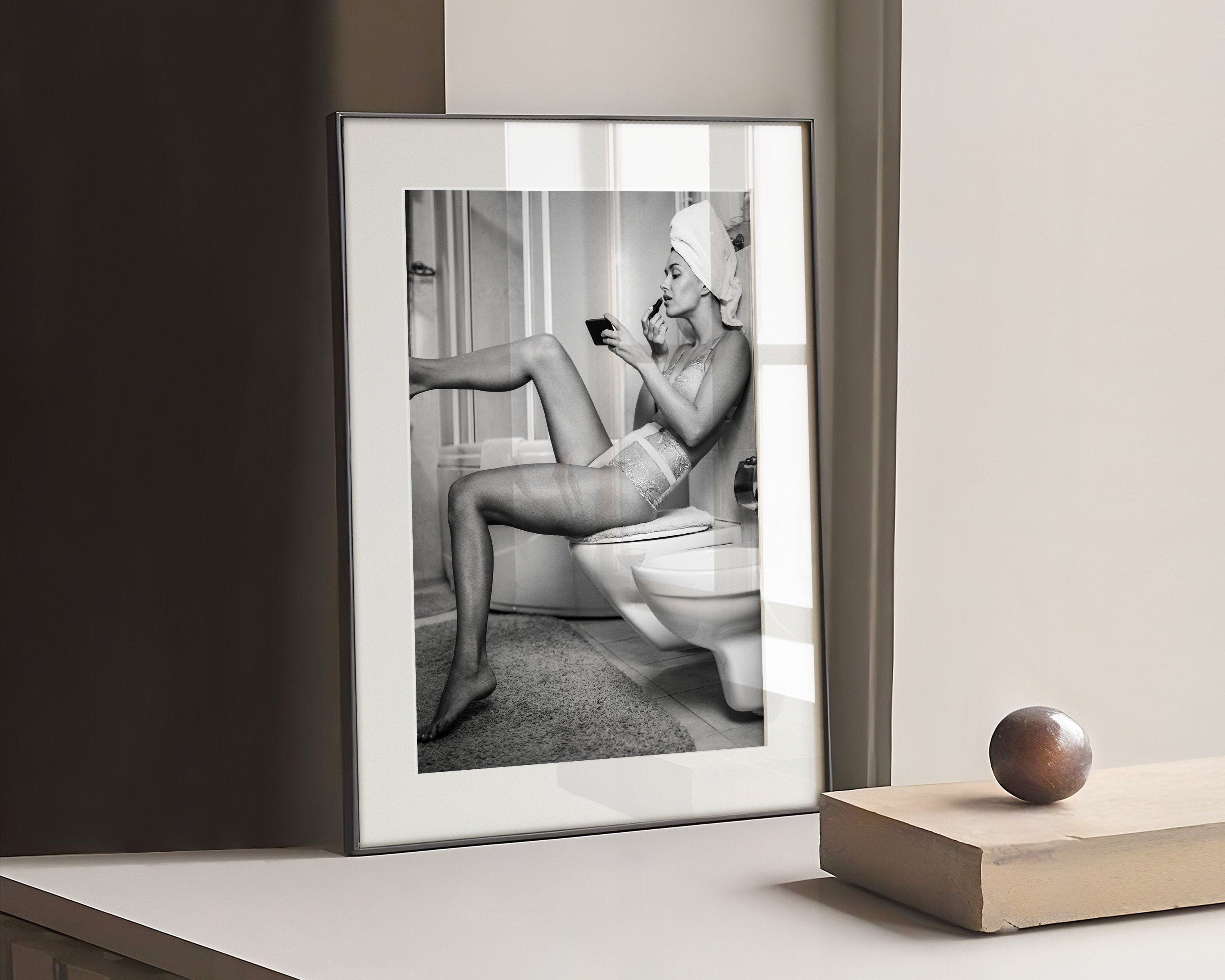 Black and white photograph of a woman resting her foot on a wall whilst putting on lipstick
