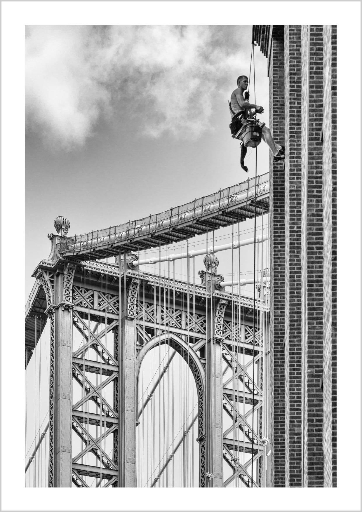 A window cleaner suspended on a rope against the Brooklyn Bridge in black and white. – Arteve Gallery