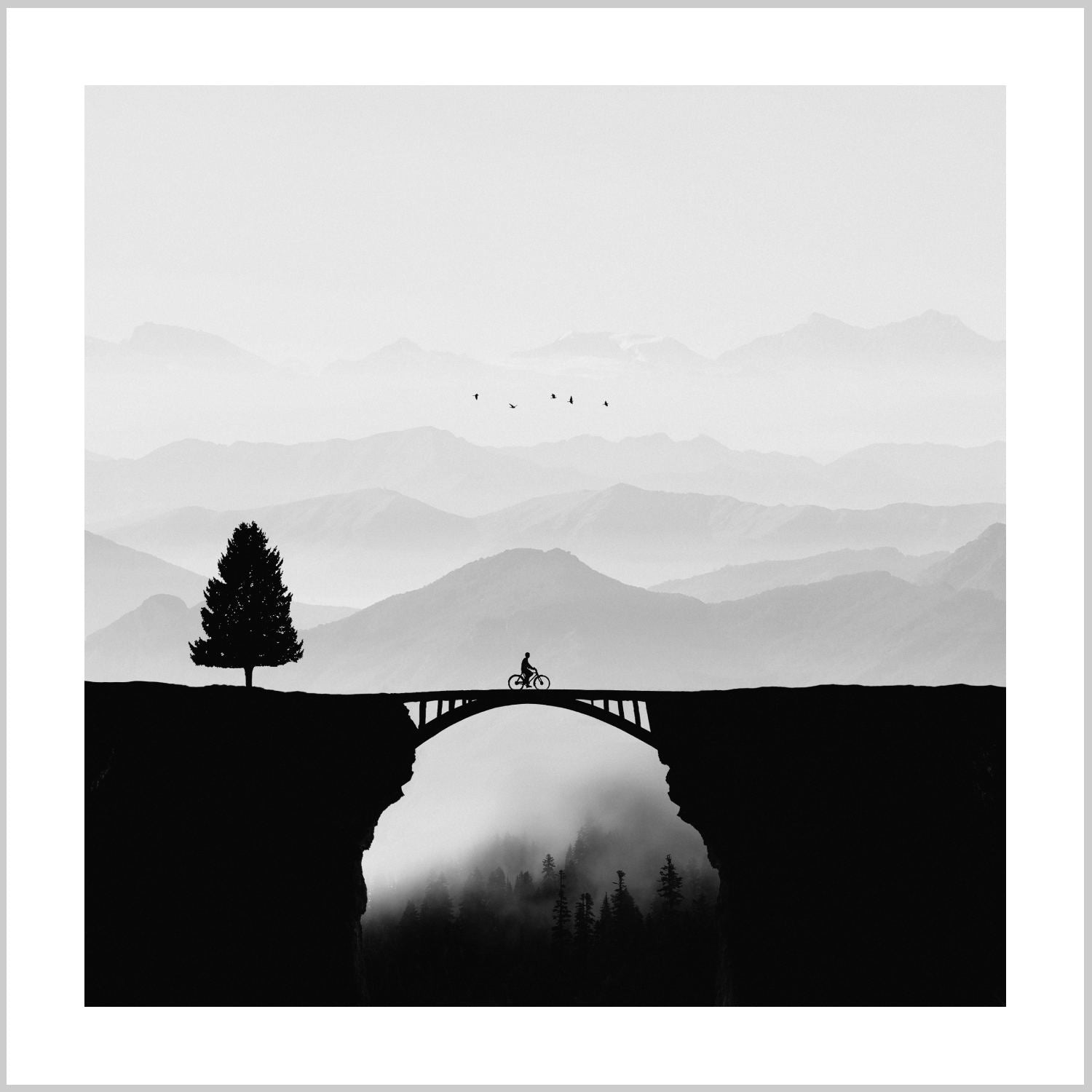 A silhouette of a cyclist on a bridge with a lone tree beside it, set against misty mountains in black and white. – Arteve Gallery